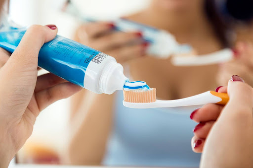 person putting toothpaste on toothbrush best oral hygiene products kneib dentistry